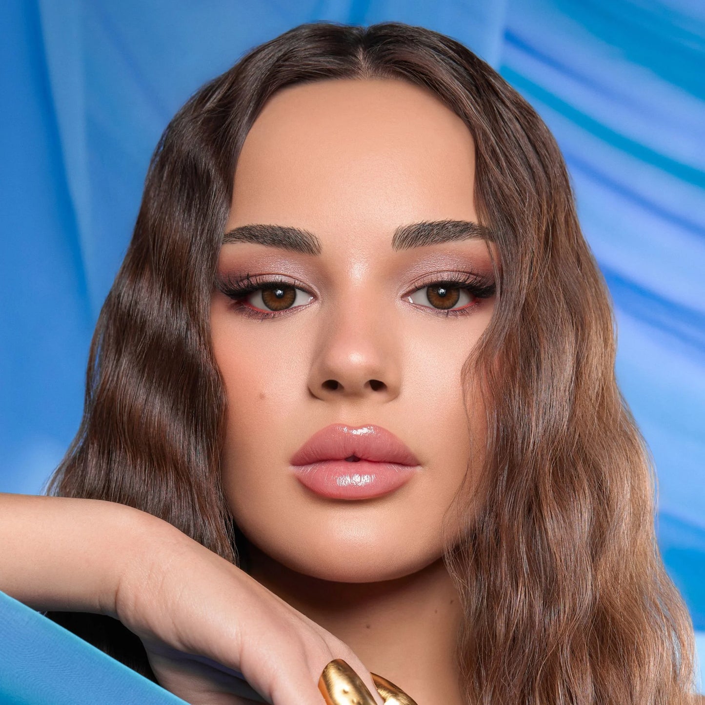 Close-up of a woman with makeup against a blue background, wearing Bella Contact Lenses named Nerelle